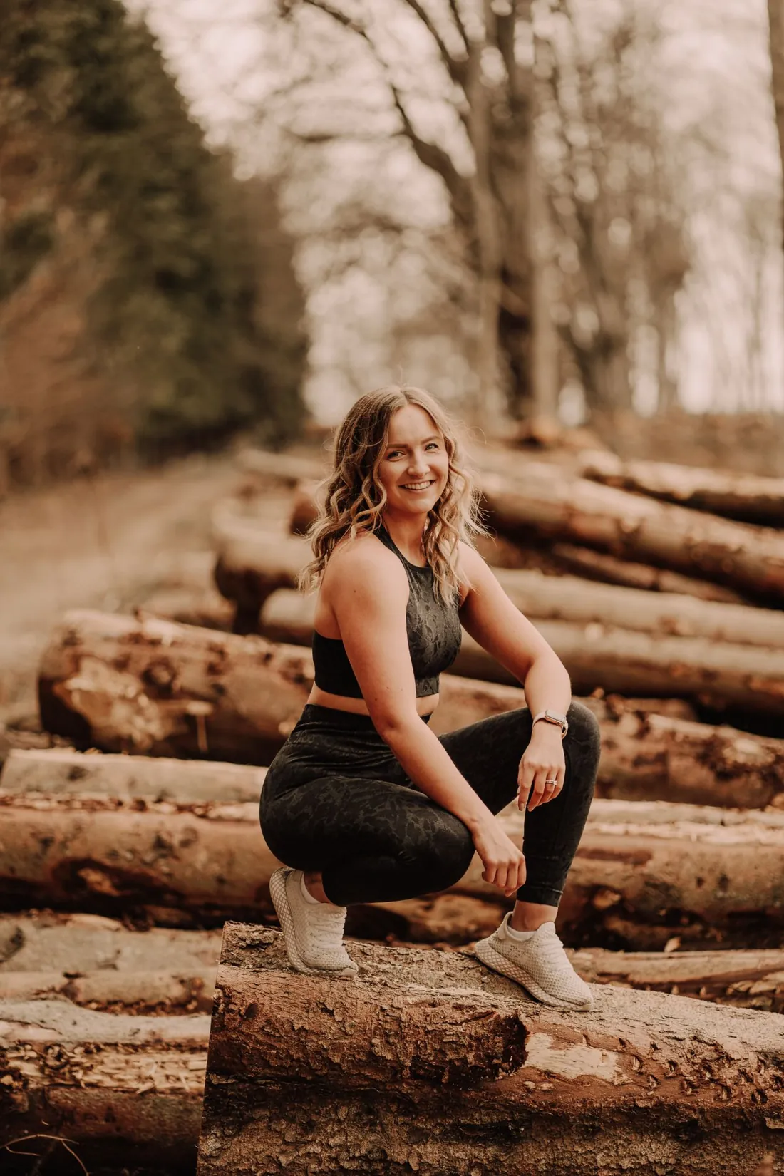 Claire crouching on a log in the woods, smiling