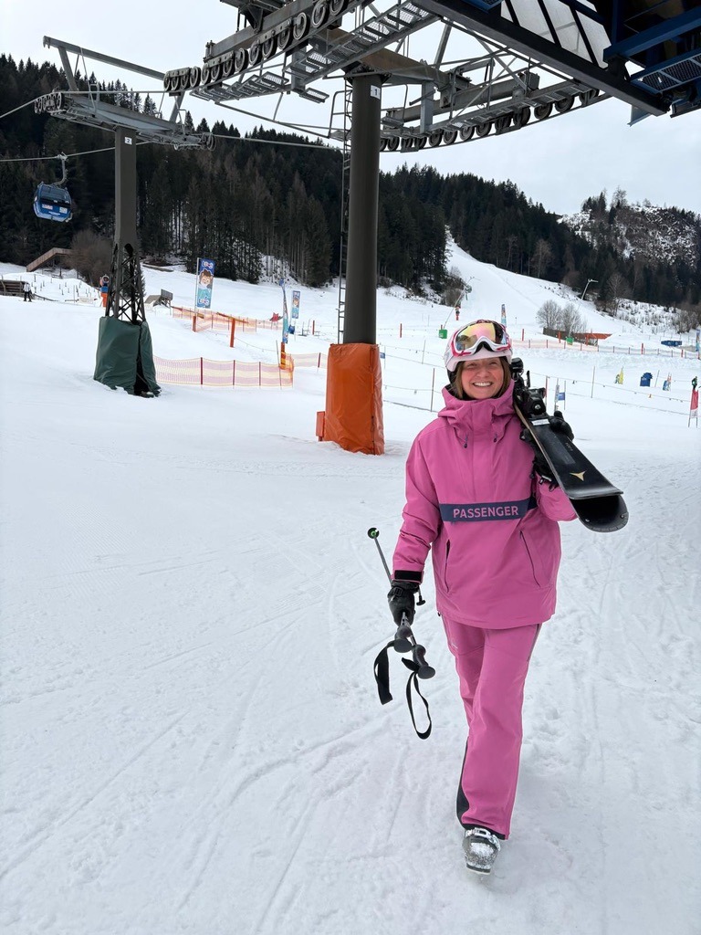 Claire in a pink ski suit carrying her skis